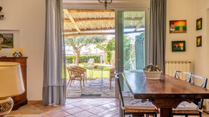 A dining area with a wooden table, chairs, and a view of an outdoor garden. - Villa Marghe - Sea View Rooms (Massa Lubrense)