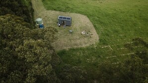 A small, single-story building with a solar panel roof, surrounded by a grassy field. - Tiny Nancy Summary:<br>H (Bellingen)