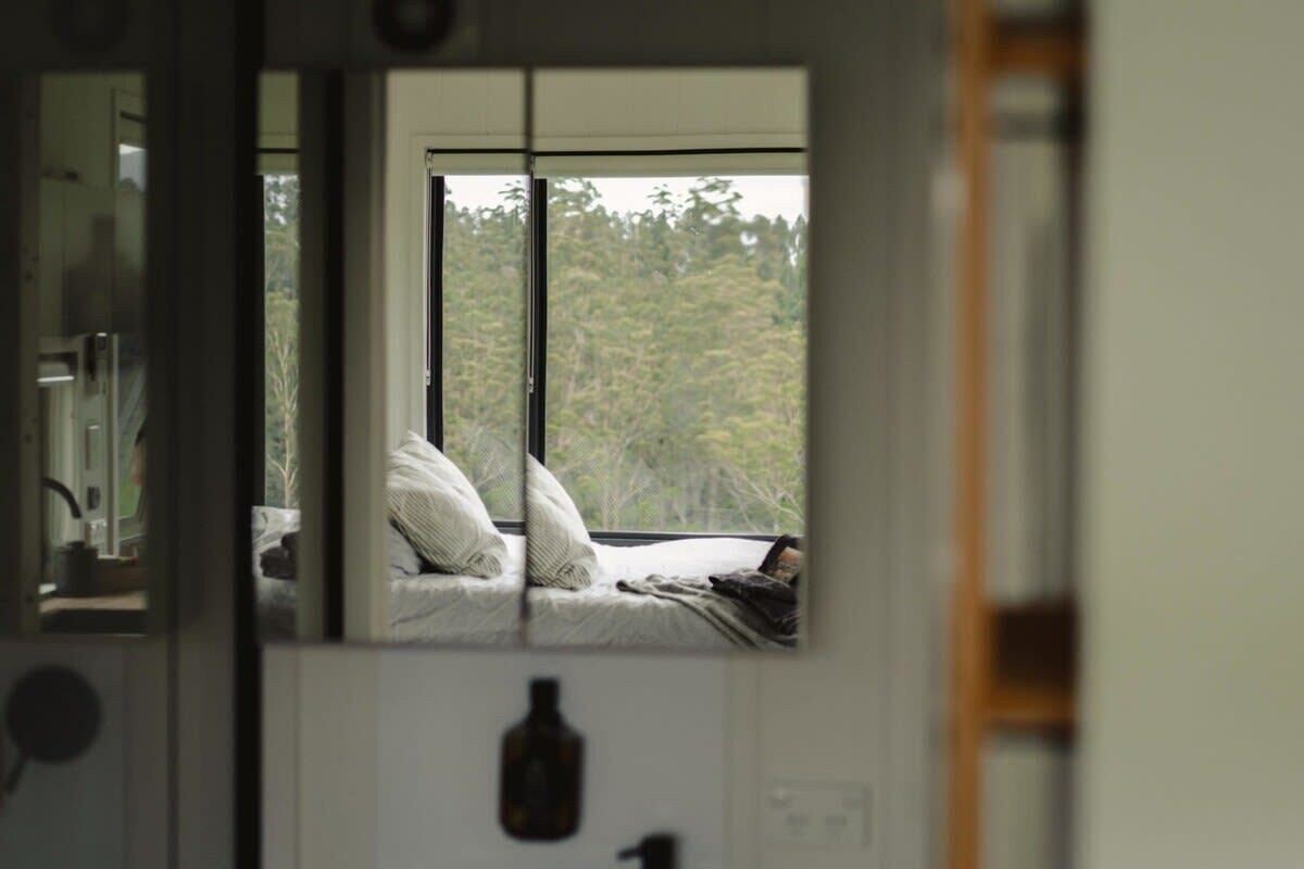 Une chambre avec une grande fenêtre, un lit avec des oreillers et une bouteille posée sur le mur.