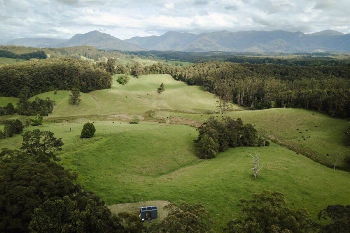 Un paysage rural caractérisé par de vastes champs verdoyants, des arbres dispersés et des montagnes lointaines.