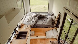 A compact RV interior with a kitchenette, a bed, and a window providing a view of the outdoors. - Tiny Nancy Summary:<br>H (Bellingen)
