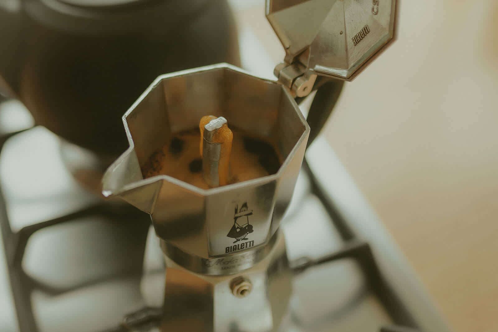 A metal coffee grinder with a logo, placed on a stove.