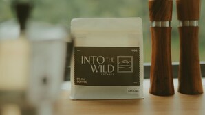 A coffee container labeled 'Into the Wild Escapes' with a weight of 150g, placed next to two wooden salt and pepper shakers on a wooden surface. - Tiny Madeline - Laguna (Markwell)