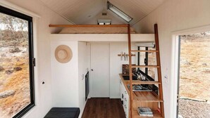 Een compacte, vrijstaande hut met een slaapzolder, een klein kitchenette en uitzicht op een droog landschap.