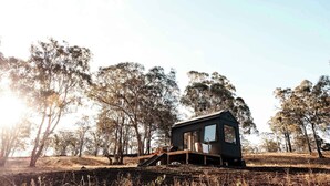 A small cabin with a wooden deck, surrounded by trees in a natural setting.