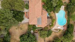 Vista aerea di una proprietà con piscina, una grande casa con tetto in tegole e vegetazione circostante.