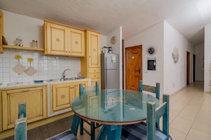 A kitchen with wooden cabinets, a glass table, and a refrigerator.