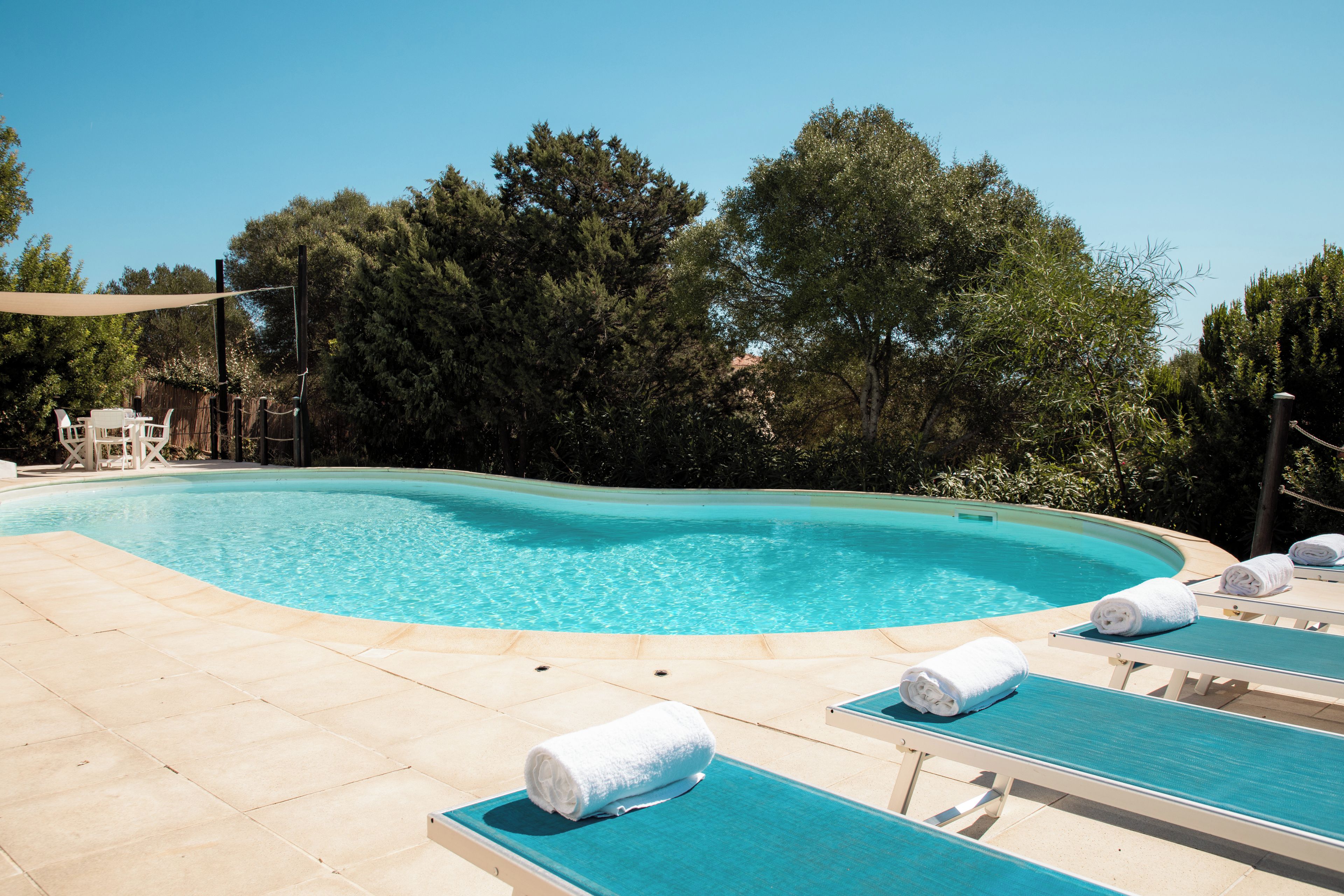 A swimming pool with lounge chairs and towels, surrounded by trees.