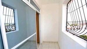 A narrow balcony with a tiled floor, a metal railing, and a view of buildings in the distance. - Lux Suites Ratna Furnished Apartments (Mombasa)