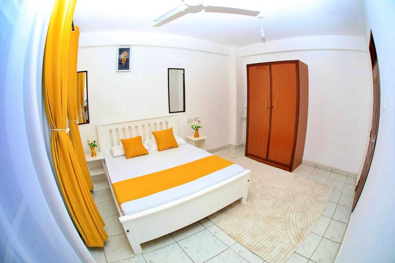 Ein Schlafzimmer mit einem Bett, einem Kleiderschrank, einem Deckenventilator und einem kleinen Nachttisch mit einer Pflanze.