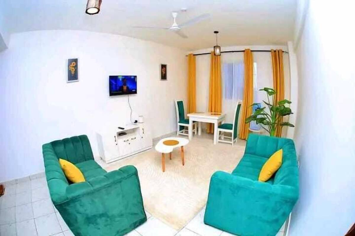 Ein Wohnzimmer mit zwei grünen Sofas, einem kleinen weißen Tisch, einem Fernseher und einem Deckenventilator.