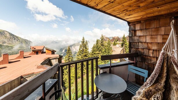 Ein Holzbalkon mit Tisch und Stühlen mit Blick auf eine gebirgige Landschaft mit Bäumen und Gebäuden.