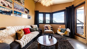 Ein gemütliches Wohnzimmer mit einer Couch, Sesseln, einem Couchtisch und einem großen Fenster mit Blick auf die Berge.