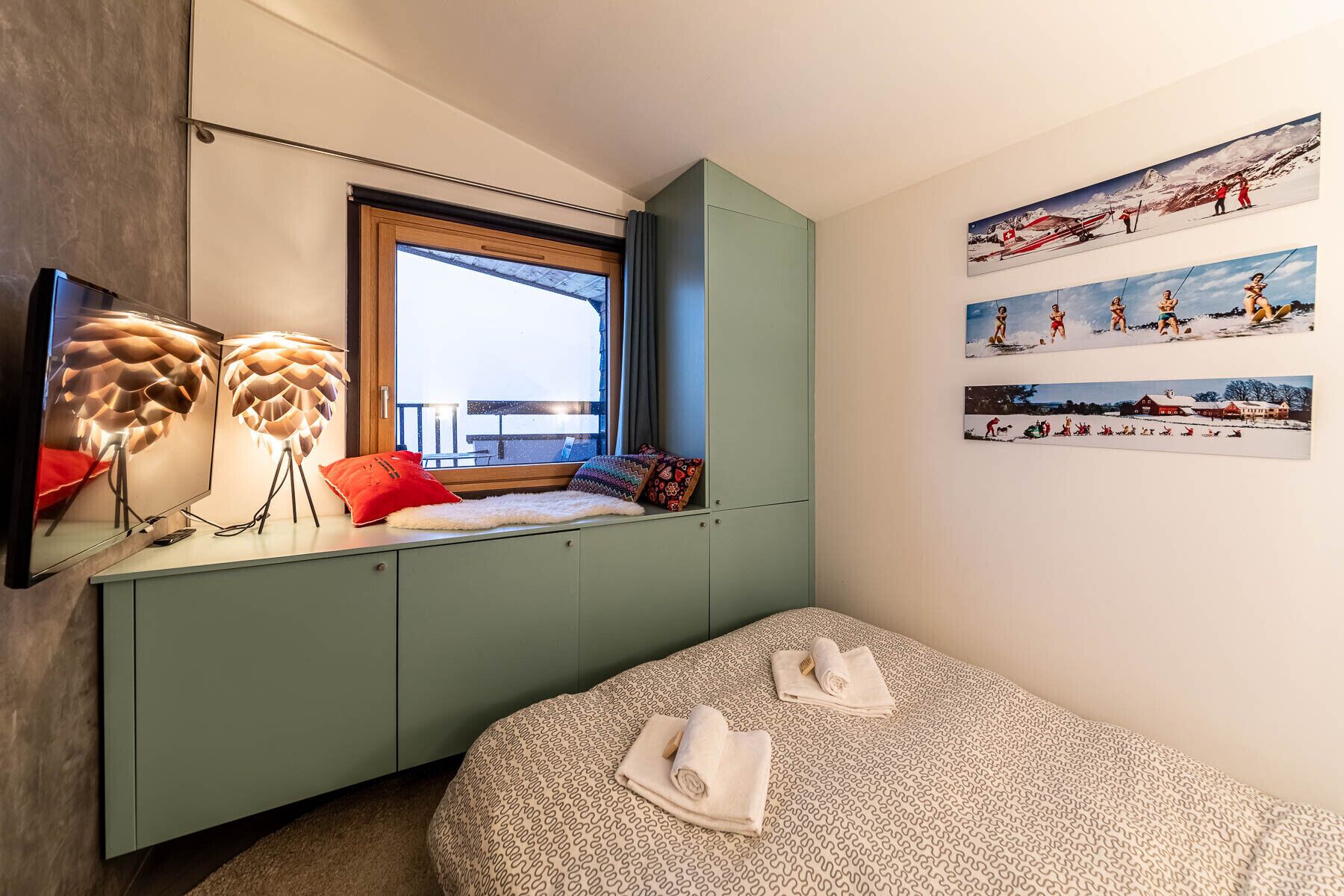 Un dormitorio con cama, ventana, espejo y obras de arte en la pared.