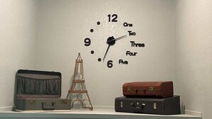 A wall clock with numbers and words for hours, a miniature Eiffel Tower, and two suitcases on a shelf. - Family Flat for 8 (Auburn)