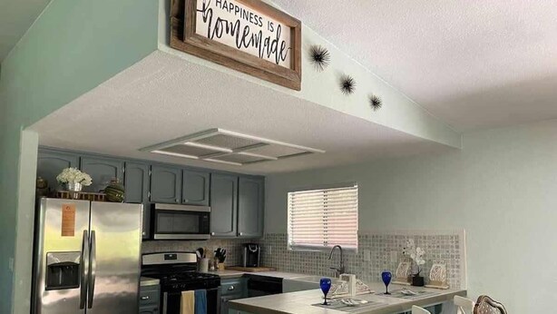 A kitchen with a stainless steel refrigerator, a built-in oven, and a sink. There is a window with blinds, a blue vase, and a sign that says "Happiness is homemade." - Family Flat for 8 (Auburn)