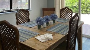 A dining area with a wooden table, four chairs, a chandelier, and a window with blinds. - Family Flat for 8 (Auburn)
