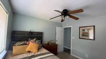 A bedroom with a bed, a ceiling fan, a door, and a framed picture on the wall.