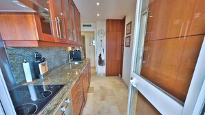 Eine schmale Küche mit Granitarbeitsplatten, Edelstahlgeräten und Holzausbau.