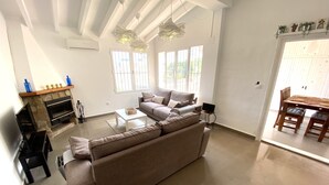 A spacious living room with a large beige sofa, a fireplace, and a dining area with a wooden table and chairs. - Casa David: Relax Cerca de la Playa (Teulada)