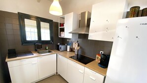 A modern kitchen with white cabinets, a black countertop, a built-in microwave, a coffee maker, and a refrigerator. - Casa David: Relax Cerca de la Playa (Teulada)