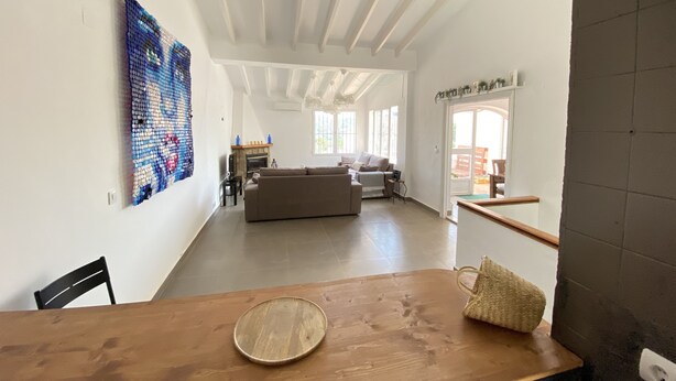 A spacious living area with a large sofa, a wooden dining table, and a colorful abstract painting on the wall. - Casa David: Relax Cerca de la Playa (Teulada)