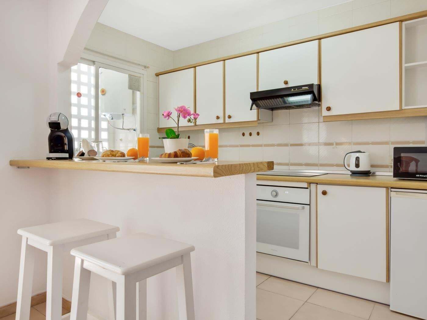 A modern kitchen with white cabinets, a coffee machine, a microwave, and a small island with stools.