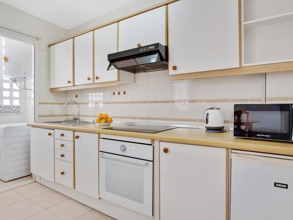 A modern kitchen with white cabinets, a built-in oven, a microwave, and a kettle on the countertop.