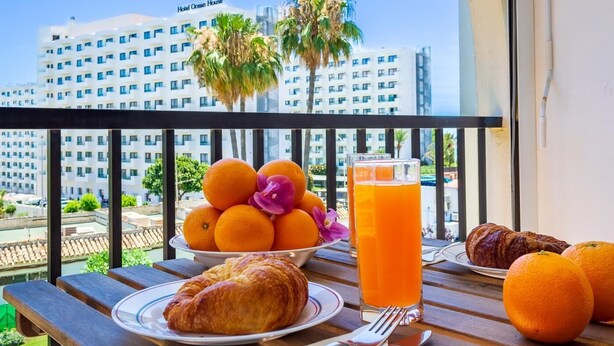 Un balcon avec une table préparée pour le petit-déjeuner, comprenant des oranges, un croissant et un verre de jus d’orange.