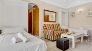 Habitación de hotel con cama, sofá a rayas, una mesita con un frutero y un escritorio con silla.