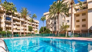 Una piscina rodeada de palmeras y un edificio de varios pisos con balcones.