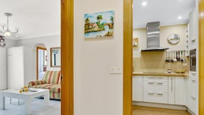 Una cocina moderna con armarios blancos, una campana extractora de acero inoxidable y un comedor con sofá a rayas y una mesa pequeña.