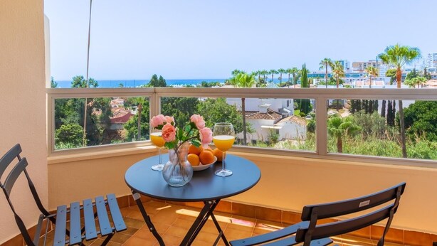 Un balcon avec une table dressée pour deux personnes, agrémenté d’un vase de fleurs et d’un saladier rempli d’oranges.