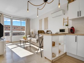 Un appartamento moderno con zona living, cucina e angolo pranzo. Dispone di un'ampia finestra, una TV a schermo piatto, un divano, un tavolo da pranzo e un bancone cucina.