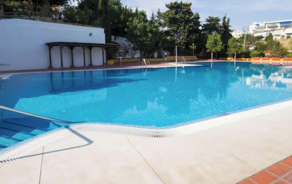 A clear swimming pool with a tiled deck, surrounded by trees and a white building. - Duquesa 703 - 2 Terraces with Sea Views, Swimming pool, Parking (Torremolinos)