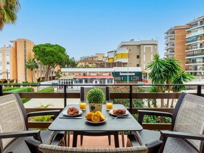 A balcony with a table set for breakfast, including croissants and orange juice, overlooking a cityscape with buildings and a restaurant.