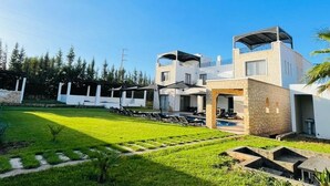 A modern multi-story building with a pool, outdoor seating, and a well-maintained lawn. - Cavanna Lodge (Ounagha)