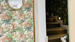 Una escalera con barandilla de madera y una pared decorada con motivos de hojas tropicales.