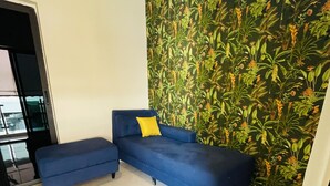 Un salón con sofá azul, alfombra gris y papel tapiz con motivos tropicales.