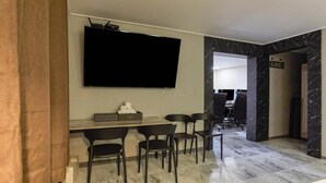 A modern living room with a flat-screen TV mounted on the wall, a coffee table, and four black chairs. - ON & OFF HOTEL (Incheon)