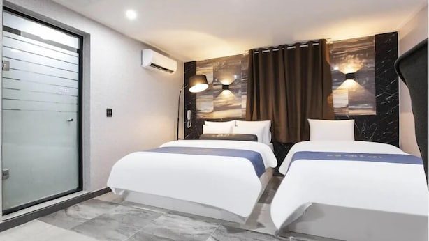 A hotel room with two beds, a sliding glass door, an air conditioning unit, and a wall-mounted lamp. - ON & OFF HOTEL (Incheon)
