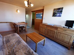 Ein gemütliches Wohnzimmer mit einer Holzdirektiva, einem Couchtisch aus Holz, einem Esstisch mit Stühlen, einer Holzkommode und einem Fernseher.