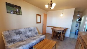 A small, cozy living area with a sofa, a wooden table, and a dining table with chairs. There is a ceiling light and a wall-mounted shelf with a lamp. - 2-bedroom apt at the foot of the slopes, balcony and elevator (Les Adrets-Prapoutel)