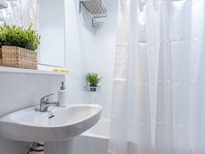 Ein Badezimmer mit weißem Waschbecken, einem Spiegel, einer Duschvorhang und einer kleinen Topfpflanze an der Wand.