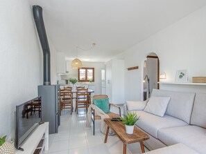 A modern living room with a sofa, a coffee table, and a television. There is a kitchen area with a dining table and chairs.