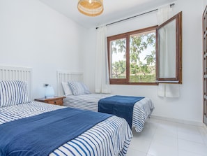 A bedroom with two beds, a window with a view, a bedside table with a lamp, and a radiator.