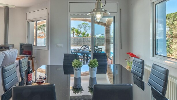 A modern dining area with a glass table, black chairs, and potted plants. - Beachside Haven with Pool, BBQ, WiFi & A/C – 200m from Sant Pere Pescador Beach (Sant Pere Pescador)