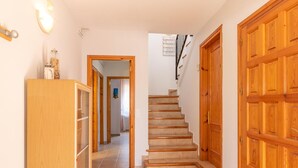 A hallway with a wooden door on the right, a wooden cabinet on the left, and a staircase leading to another room. - Beachside Haven with Pool, BBQ, WiFi & A/C – 200m from Sant Pere Pescador Beach (Sant Pere Pescador)