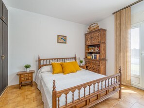 Ein Schlafzimmer mit einem hölzernen Bett, einem Nachttisch, einem Holzschrank und einem Fenster mit Vorhängen.