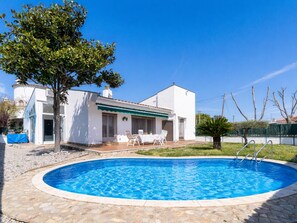 Ein Poolbereich mit Pool, ein weißes Gebäude mit grüner Markise und ein Baum.